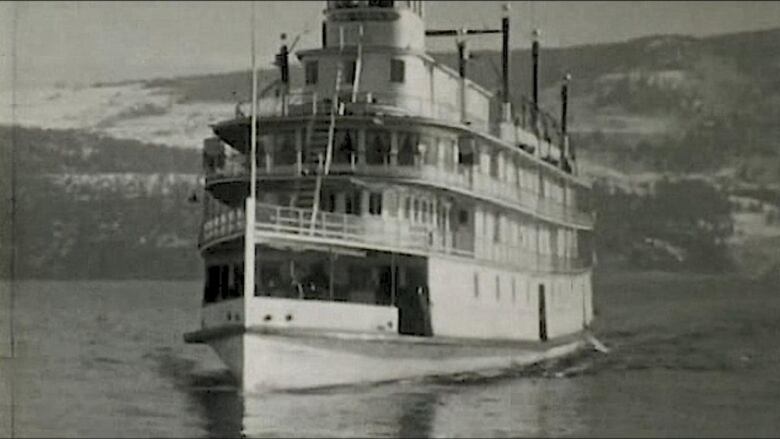 A steam ship sails in the lake, with hills in the background.