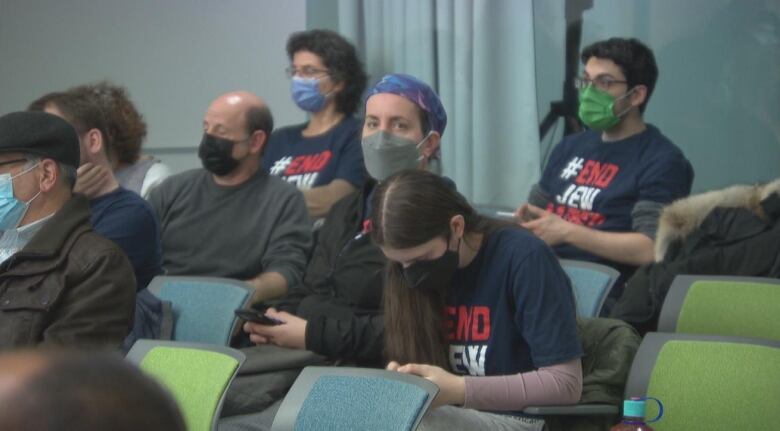 Masked people in chairs at a meeting.