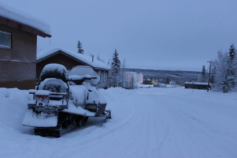 A parked snowmobile on a snow-covered road in the low light of dawn.