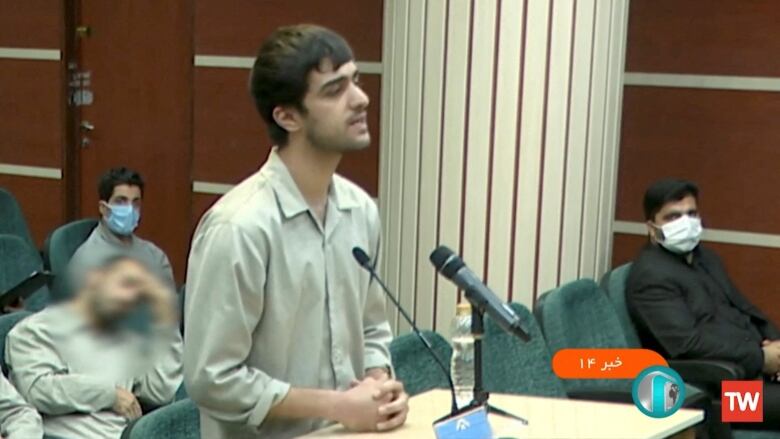 A man speaks at a microphone during a courtroom appearance.