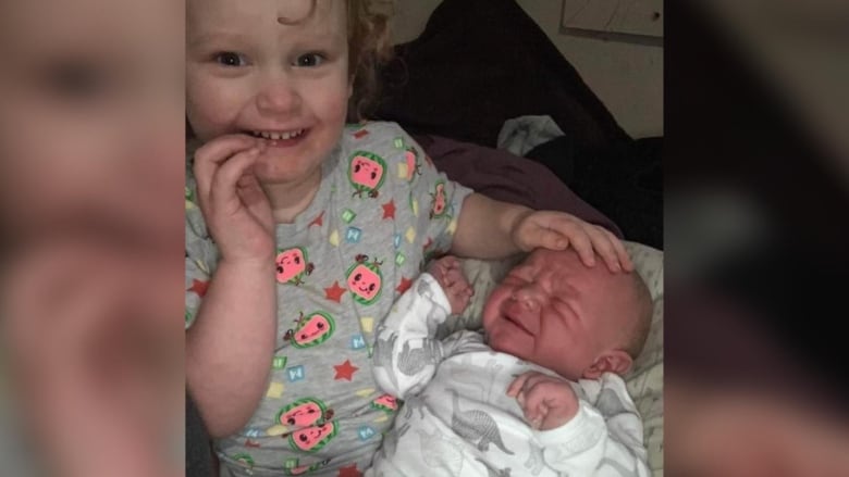 A toddler sits with a newborn baby.