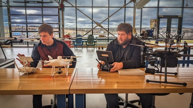 Two men holding drones in a large open room 