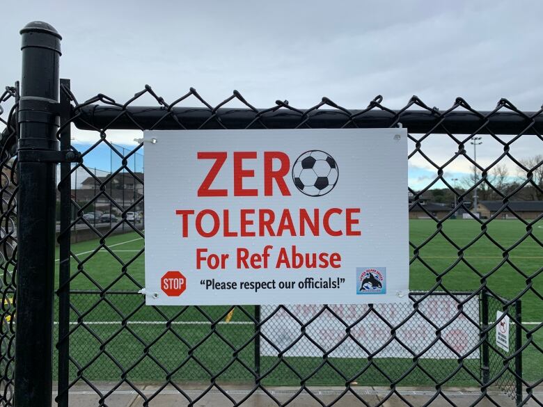 A sign attached to a fence at a soccer field reads 