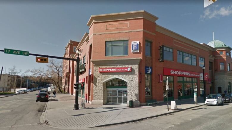 A two-storey corner store with a sandstone entrance and red brick exterior has a bright red sign that reads Shoppers Drug Mart.