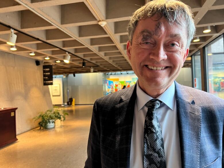 A man stands in the hallway of an art gallery, smiling at the camera. 