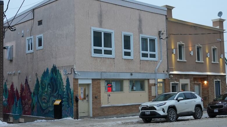 A beige building on a downtown street with a green mural on the side.