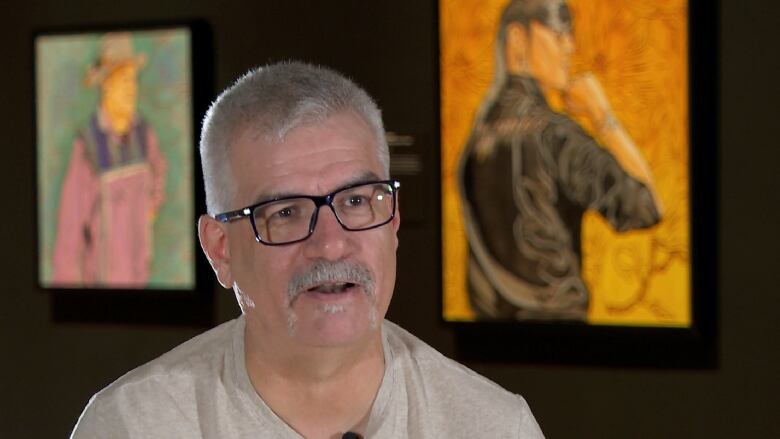 A man sits in an art gallery with two colourful paintings in the background.