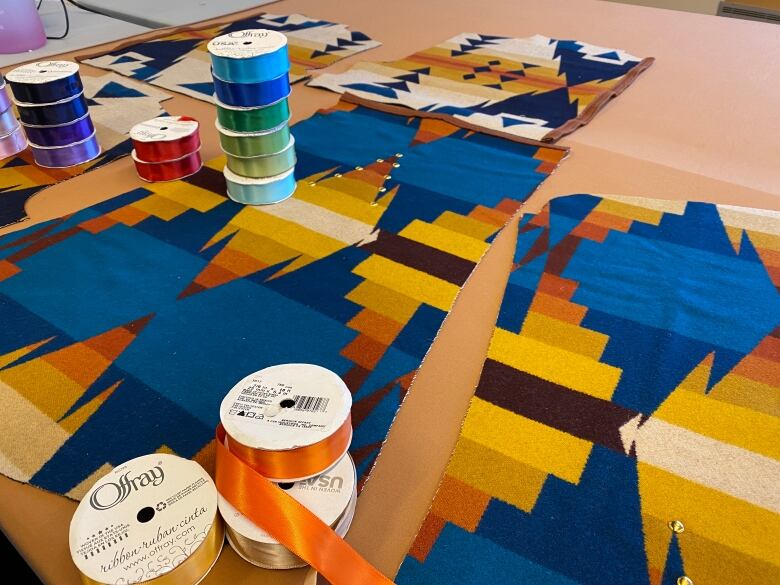 Fabric is layed out on a table with spools of colouful ribbon placed on top of it.