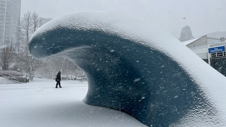 Halifax wave sculpture covered with snow. A person is seen walking in the background.