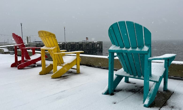 Colourful deck chairs on the Halifax waterfront facing the water are shown covered with snow.