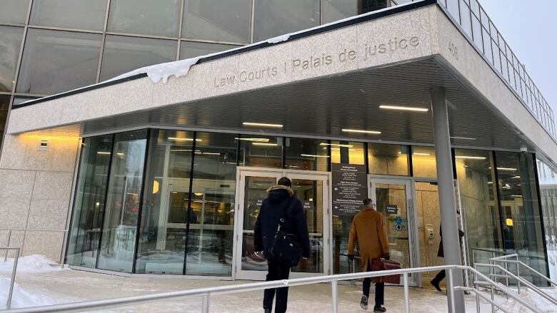 A person in a black winter coat and another in a brown coat enter a building with the words Law Courts inscribed above a set of doors.