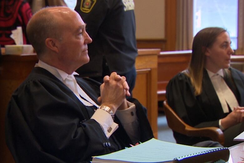 Two people wearing lawyers robes are sitting in a court room.