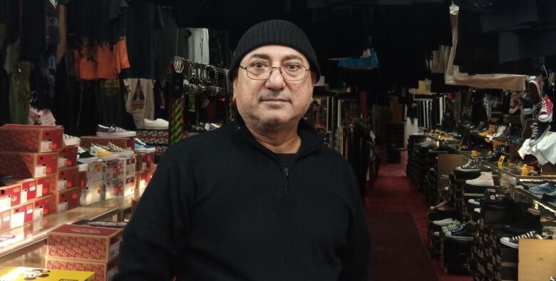 A person in black and a black tuque stands in a store full of t-shirts and cool sneakers.