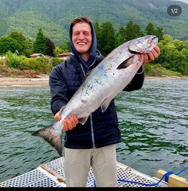 Tsekhmistrenko has a big smile on his face as he holds up a large fish near water.