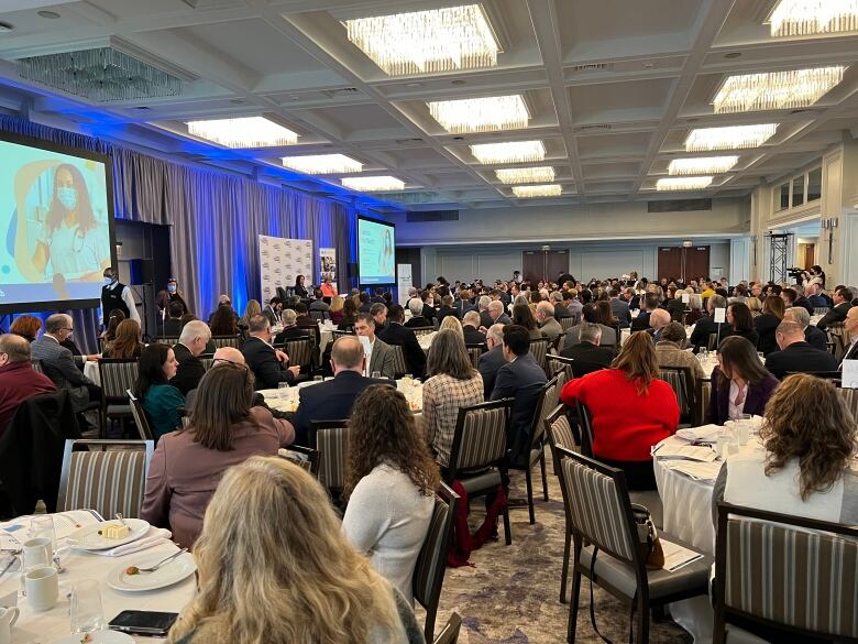 People sit at round tables in a large room during a business luncheon.