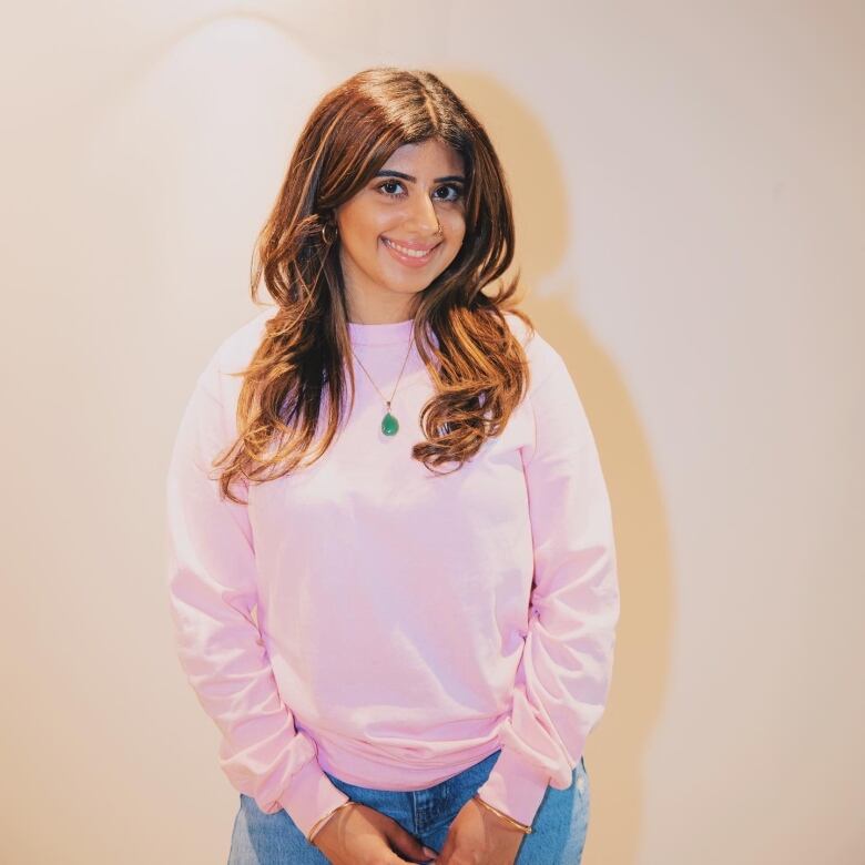 A girl wearing a pink sweatshirt and jeans smiles for the camera