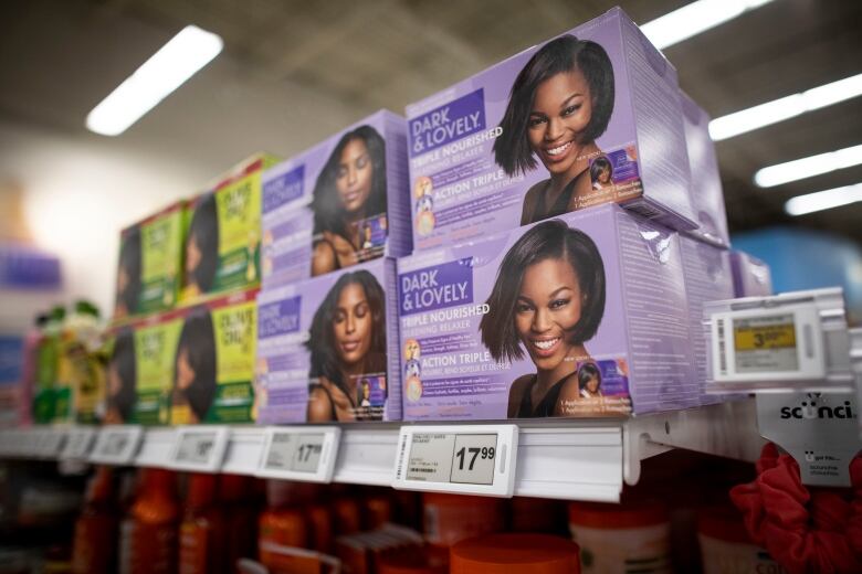 Purple boxes reading 'Dark & Lovely' that depict a smiling young Black woman with a straight bob hairstyle are shown stacked on a grocery store shelf.