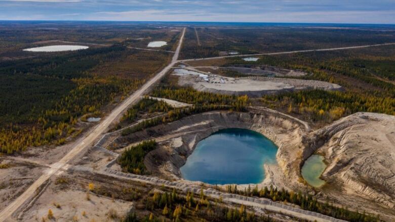 An open pit of water stands against great forest with a body of water in the distance. 