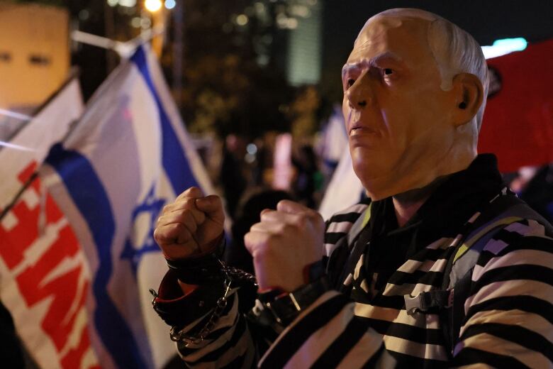 A man wearing a face mask and black and white striped costume stands in a crowd of protesters.