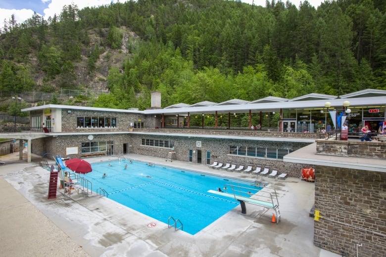 A swimming pool, surrounded by a balconies with a restaurant and green hills.