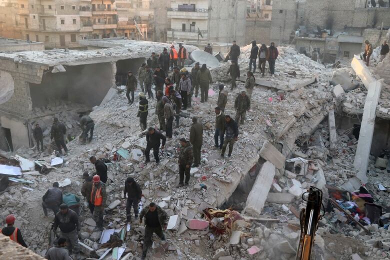 Emergency workers stand in the rubble of a collapsed building.