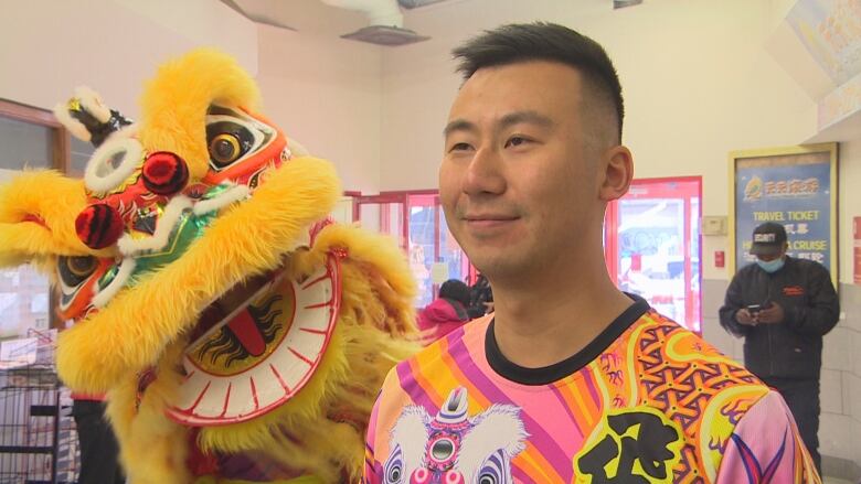 A man stands with a lion costume behind him.