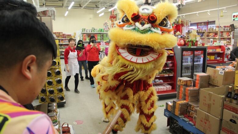 Two people in a lion costume are walking through a supermarket, while a drum is played in the foreground.