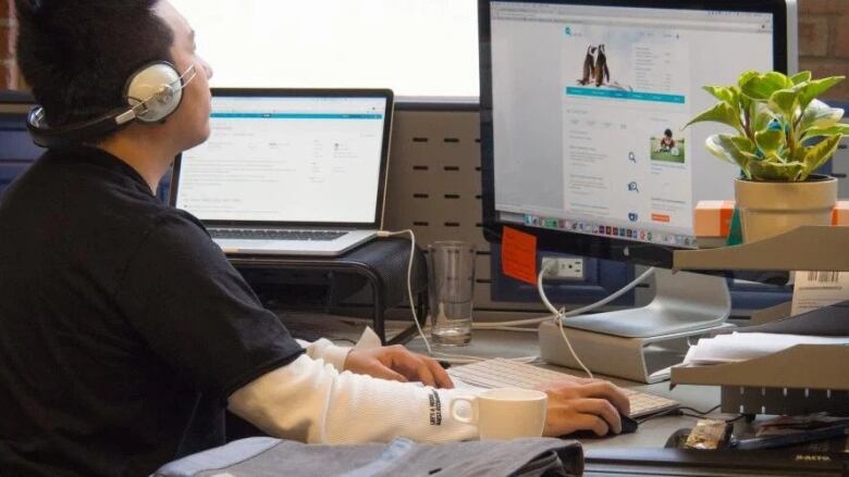 A man sits at a desk wearing headphones looking at a computer.