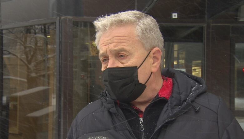 A man in short, white hair and a black face mask looks off to the left of a photograph that shows his face and shoulders.