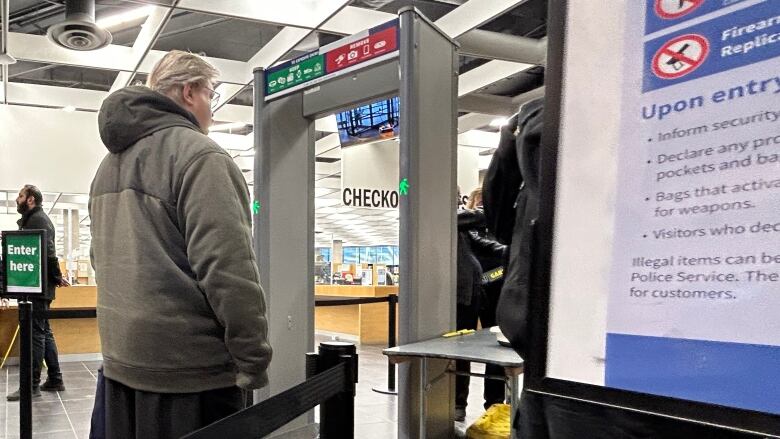 A person in a grey hooded jacket waits to go through a metal detector.