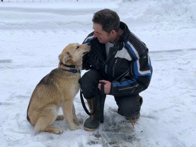 A man leaning next to a light-coloured dog.