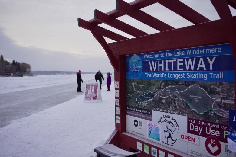 An ice skating trail with people on it, with a sign in front of them that reads 'Whiteway: the World's longest skating trail.'