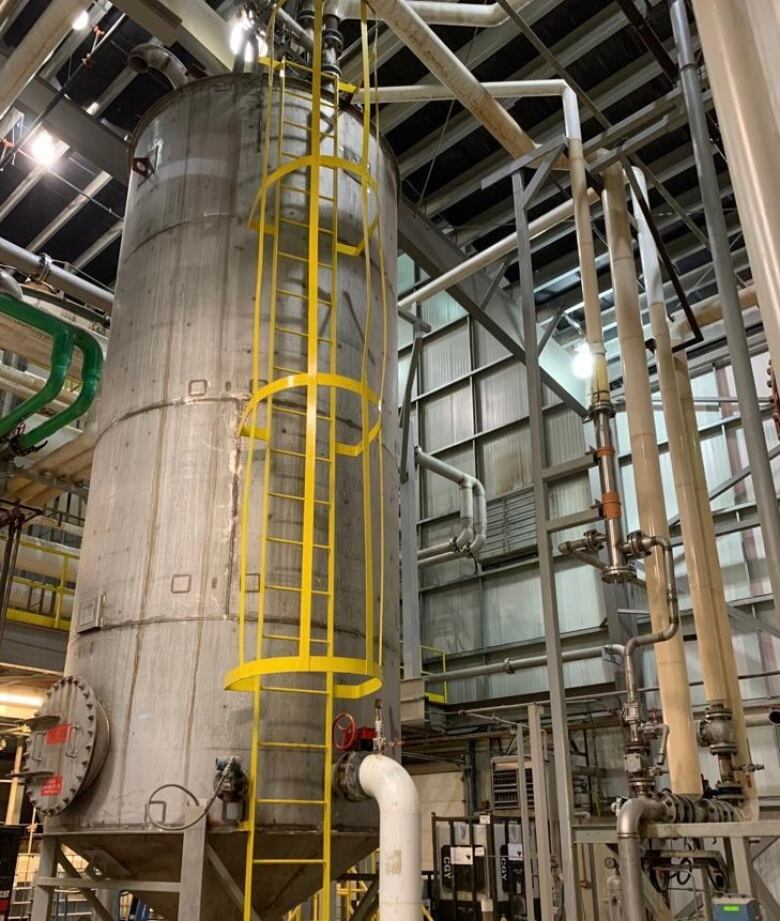 A tall, cylindrical, metal tank stands in a large industrial building.