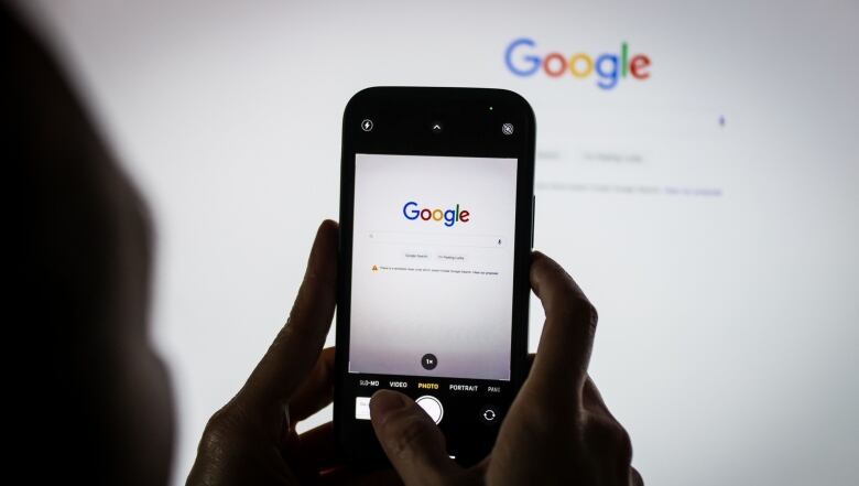 The Google logo on the company's homepage, arranged on an iPhone and a desktop computer in Sydney, Australia, on Friday, Jan. 22, 2021. Google threatened to disable its search engine in Australia if its forced to pay local publishers for news, a dramatic escalation of a months-long standoff with the government. Photographer: David Gray/Bloomberg