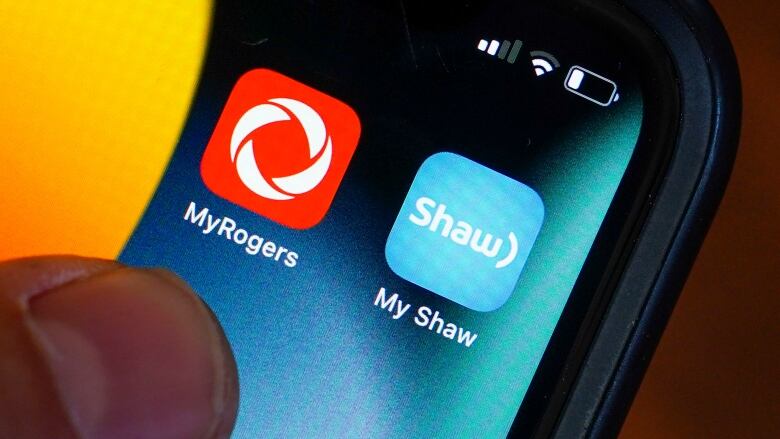 A cellphone with apps for two telecom firms Rogers and Shaw are shown.