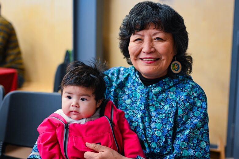 Smiling woman in red lipstick holding small child also in red. 