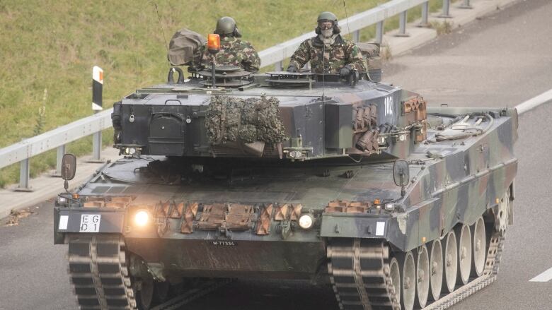 A military tank with two individuals on board.