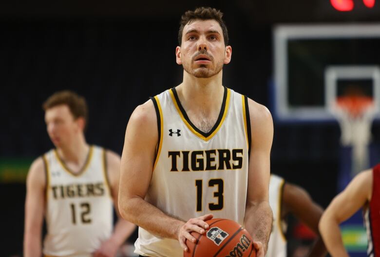 A male basketball player in a white uniform prepares to take a foul shot.