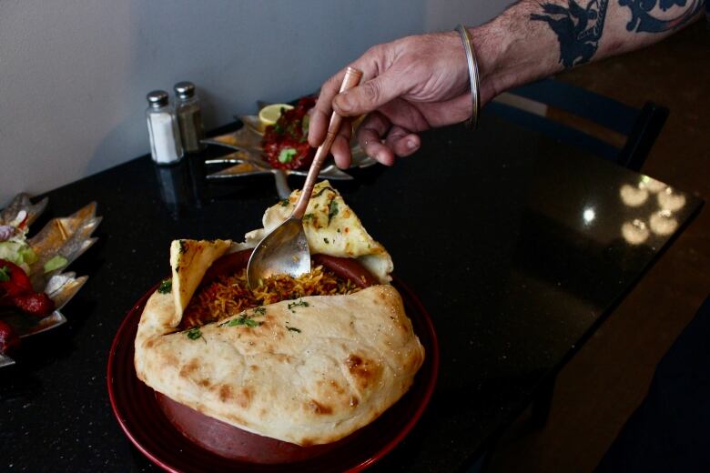 An outstretched hand uses a spoon to open the flatbaread covering a bowl of rice.