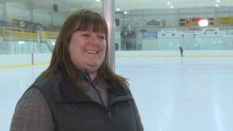 A woman standing, smiling in front of an ice rink. 