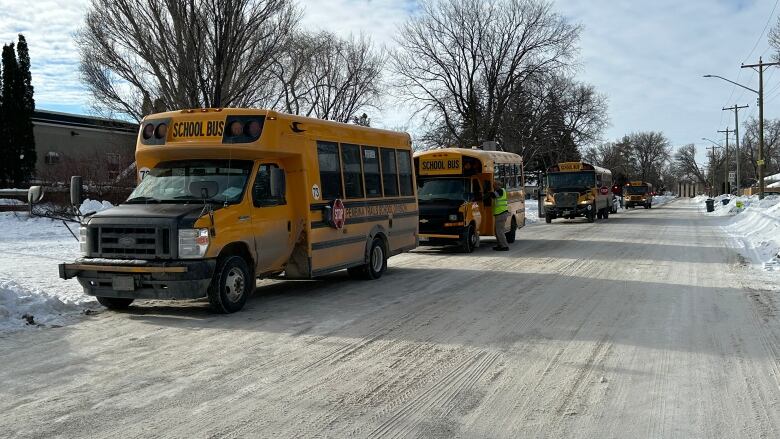 Four yellow school buses are parked on a snow-covered road on a winter day with partly cloudy skies.