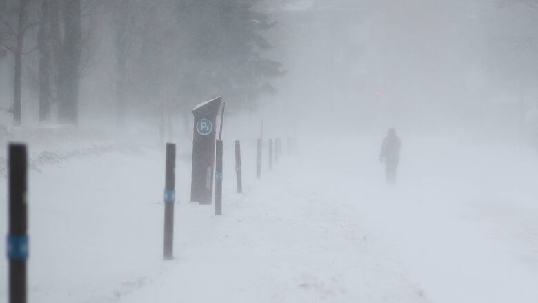 A barely visible person walking in the snow. 