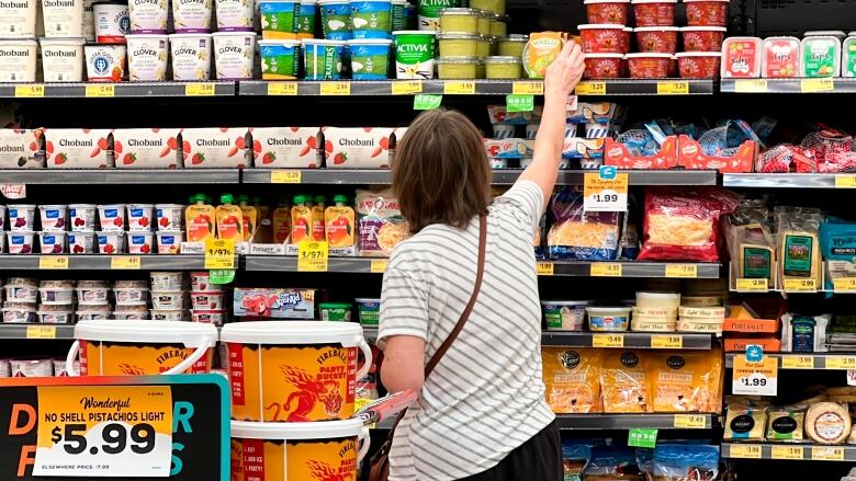 A woman reaches up for a container at a grocery store fridge containing cheese, fruit and yogurt.