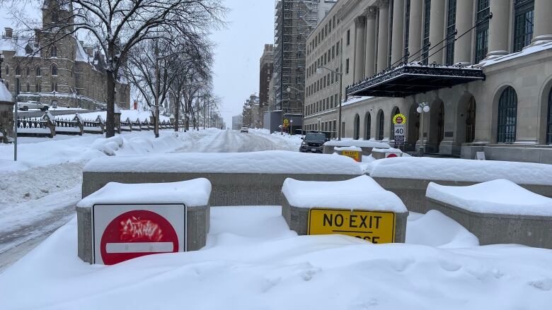 Concrete barricades designed to prevent vehicles from accessing a downtown street are seen covered in snow.