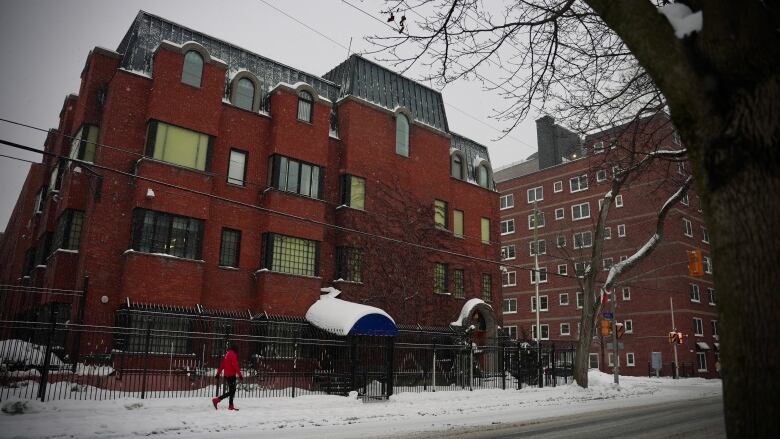 A pedestrian walks in front of a red brick building on a winter day.