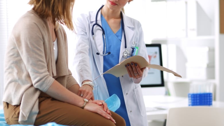 A doctor checks the pulse of a female patient as she sits on an examination table.