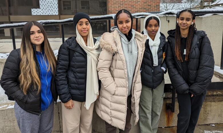 5 students stand in a row smiling