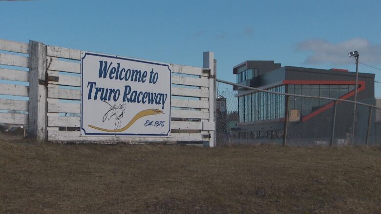 A sign that reads Welcome to Truro Raceway hangs on a white fence. A viewing grandstand sits in the distance.