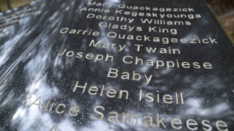 The woods are reflected on a stone listing the names of children buried in the cemetery at the former St. John's Residential School 