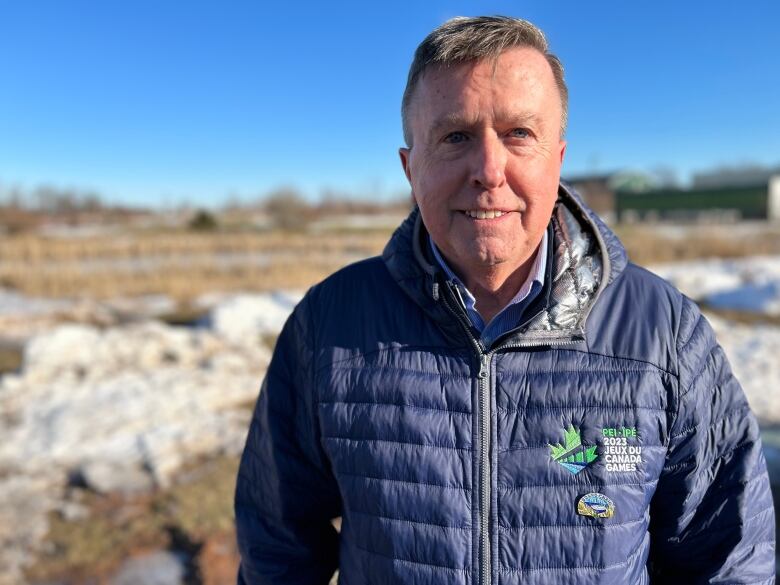 A portrait of a man standing outside, wearing a jacket with the Canada Winter Games logo. 